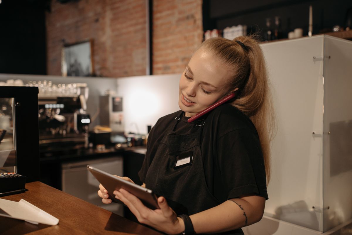 Una barista al bancone del proprio locale, tablet alla mano